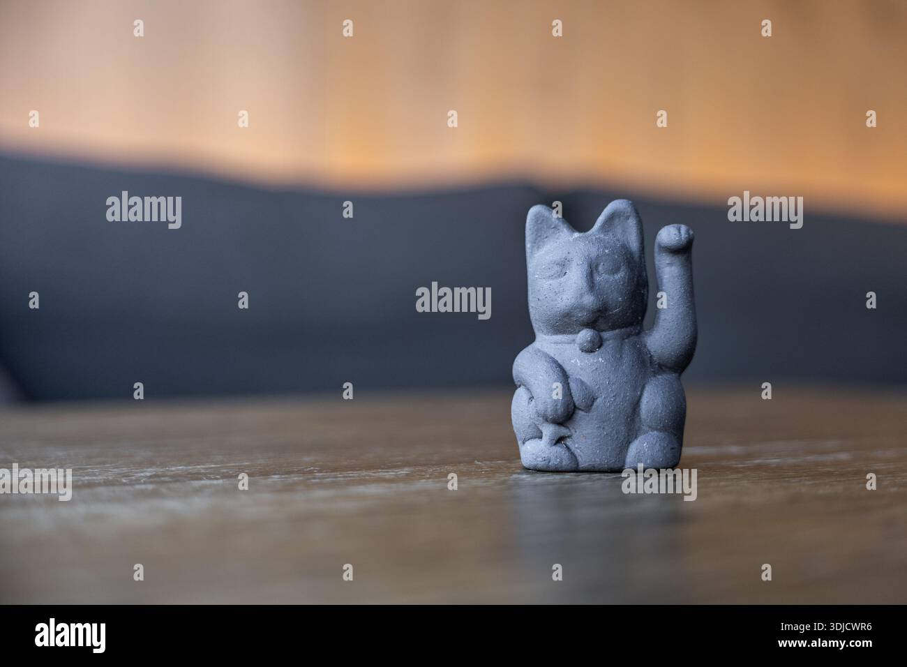 Eine schwarze Keramikkatzenfigur mit erhobener Pfote sitzt auf einem Holztisch. Der Hintergrund ist sanft verschwommen und schafft eine warme Atmosphäre. Stockfoto