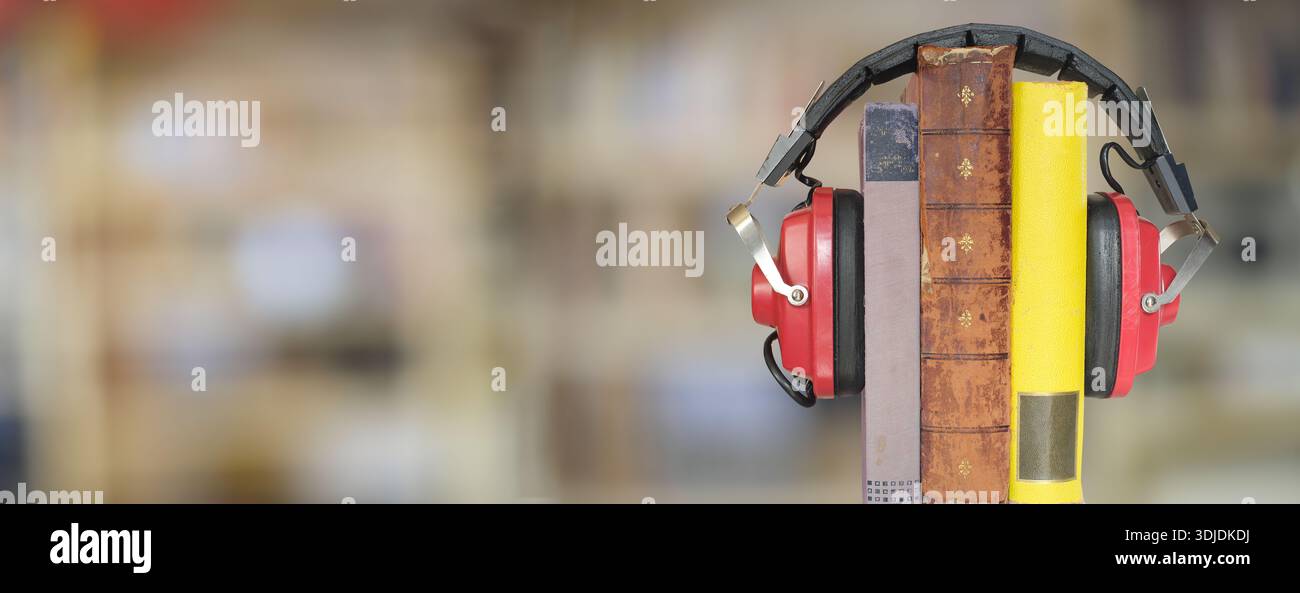 Hörbücher, Podcast, Literaturkonzept. Bücherreihe mit Vintage-Kopfhörern und verschwommenem Bücherregal im Hintergrund. Freier Kopierbereich Stockfoto