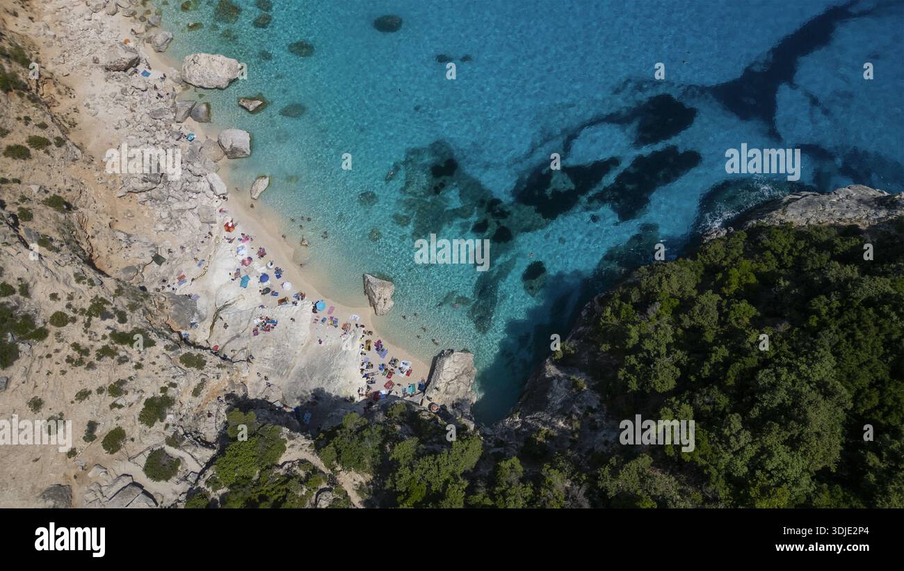 Aus der Vogelperspektive auf das türkisfarbene Meer, das die zerklüftete Küste küsst, wo sonnenverwöhnter Sand auf üppige grüne Klippen trifft, ein malerischer Kontrast, der von oben sichtbar ist Stockfoto