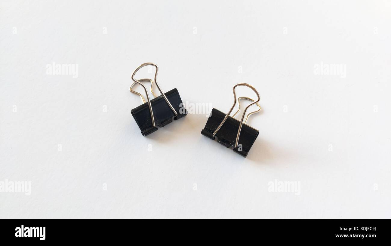 Binder-Clips auf weißem Papier, Bulldog-Clips, Schreibwaren-Clips aus schwarzem Metall werden isoliert auf weißem Hintergrund angeordnet. Stockfoto