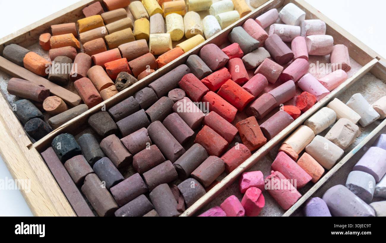 Verschiedene Stifte aus weichem Pastellfarben im Holzkoffer. Rosafarbene, rote, gelbe, braune Stäbchen. Mehrfarbiger Hintergrund. Kreideteile, Draufsicht. Kunstfarbe Stockfoto