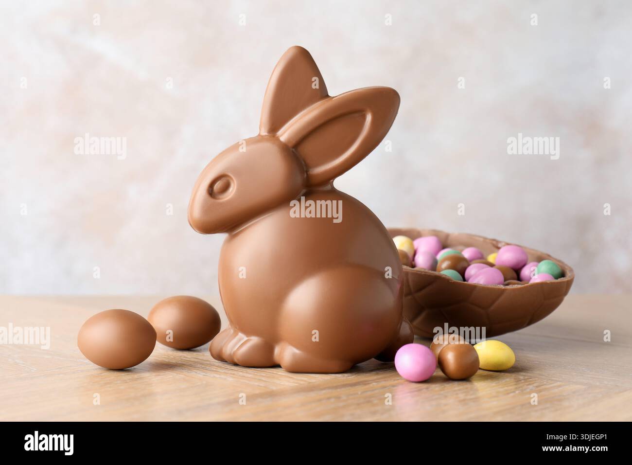 Schokoladen-Osterhase und Ei auf Holztisch vor hellgrauem Hintergrund, Nahaufnahme Stockfoto
