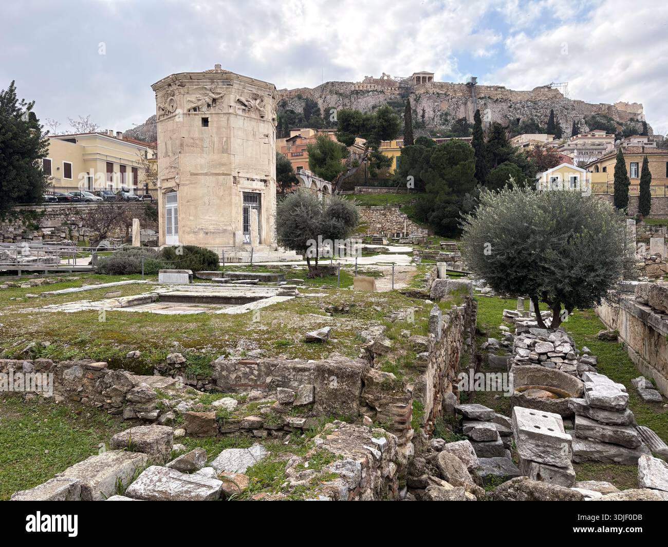 Der Turm der Winde (Horologion von Andronikos) in der Nähe von Hadrian's Library, Antike Agora, Athen, Griechenland. Blick über grasbewachsene Ruinen in Richtung Akropolis Stockfoto