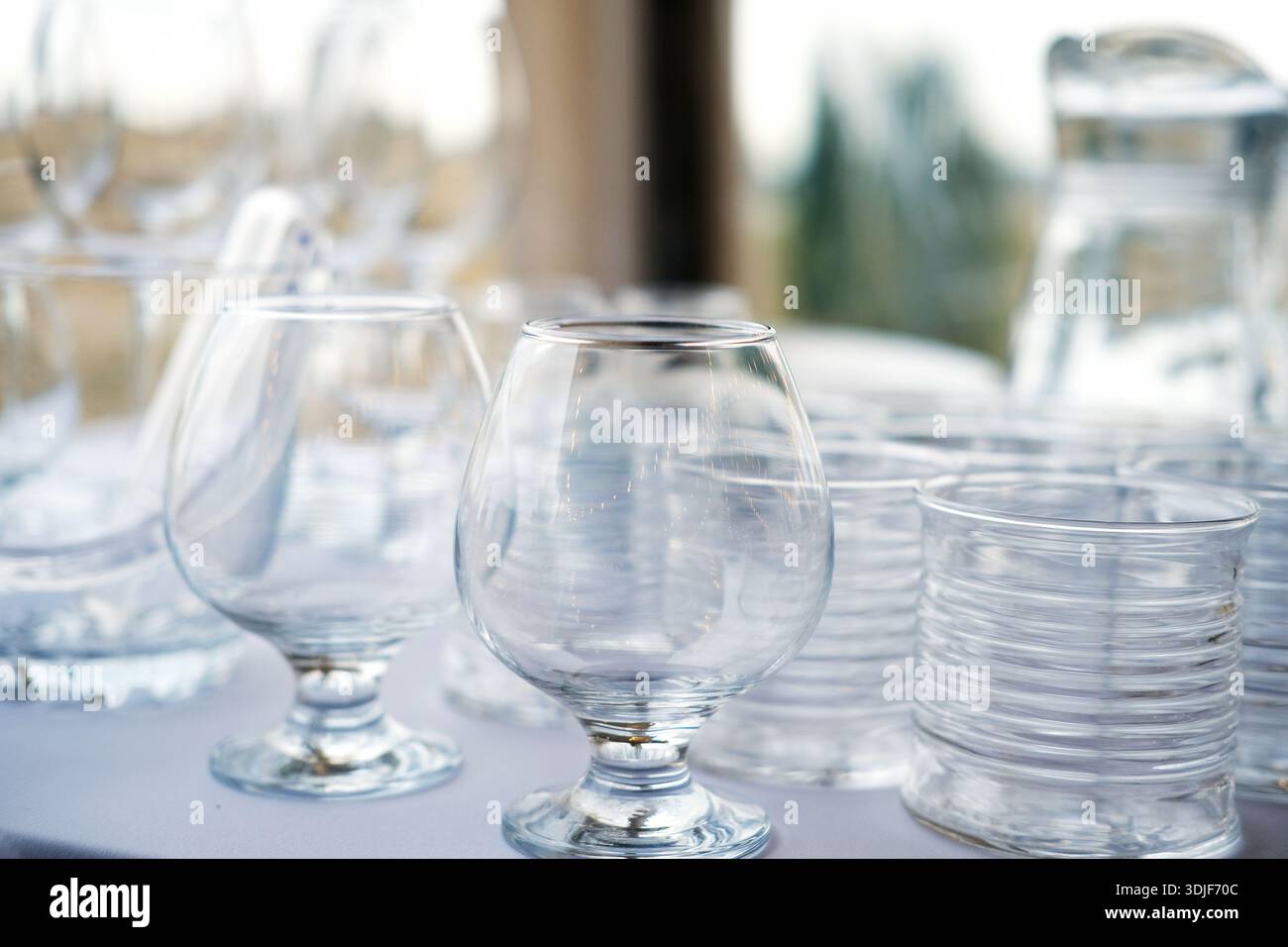 Sammlung klarer Glaswaren, einschließlich Stielgläser und Trinkgläser, die auf einem Tisch angeordnet sind und Transparenz und Reflexionen in einem gut beleuchteten umfeld hervorheben Stockfoto