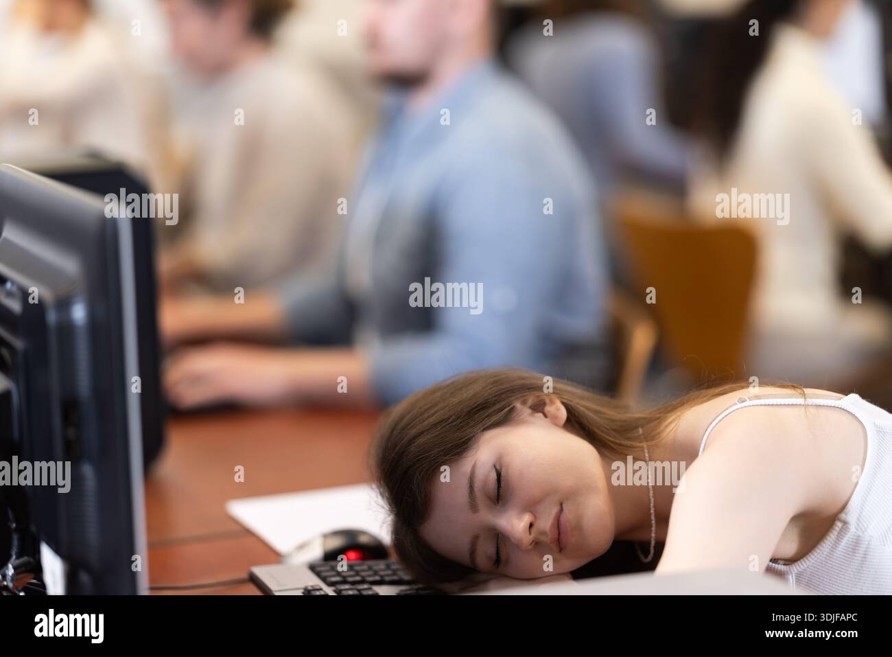 Junge Studentin schläft während der Fortbildung im Computerlabor ein Stockfoto