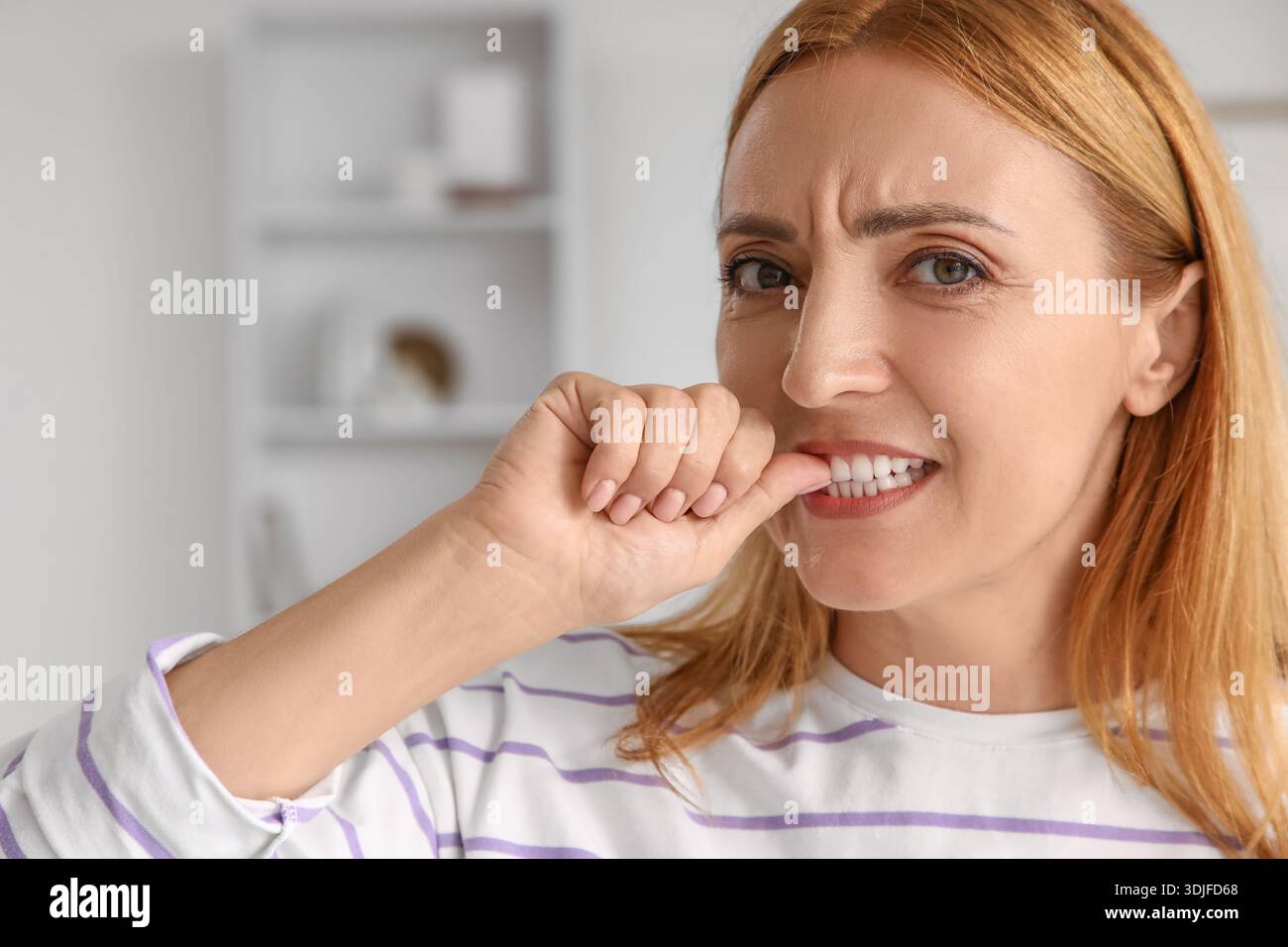 Besorgte reife Frau beißt zu Hause Nägel Stockfoto
