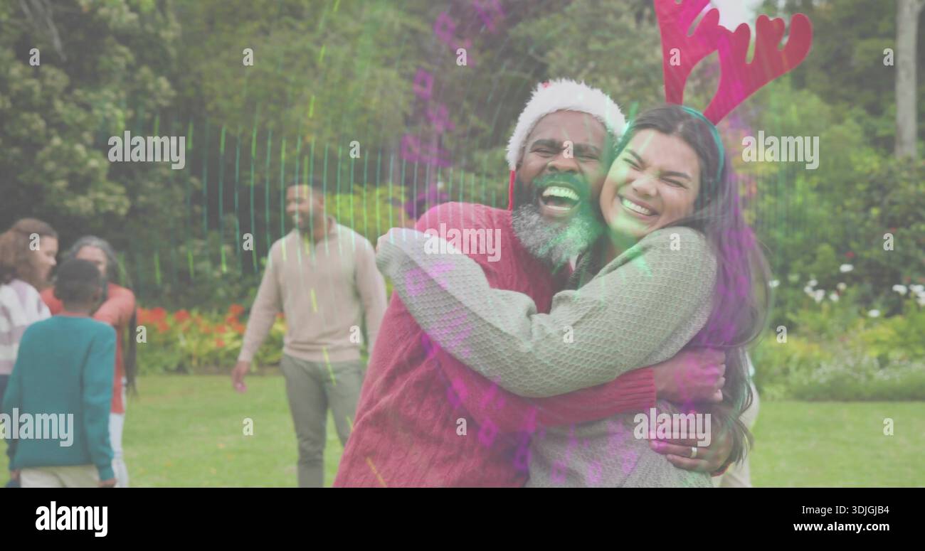 Umarmt reifes Paar, lacht auf dem Rasen im Park, trägt Weihnachtsmütze, Geweih, Stricke, Lichtringe Stockfoto