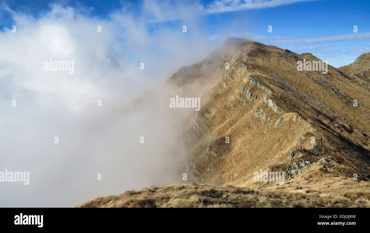 Eine dramatische Weitwinkelaufnahme des steilen, felsigen Berges des Mount Braiola, von den Hängen des Mount Marmagna aus gesehen, mit einem dicken Wolkenmeer. Stockfoto