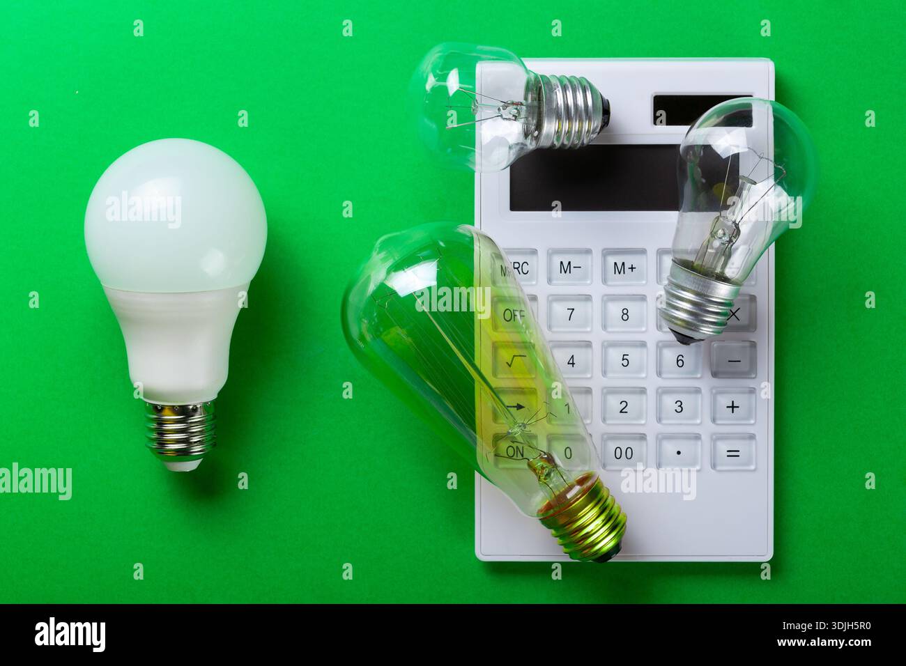 Weißer Taschenrechner und LED-Lampe auf grünem Hintergrund. Konzept zur Zahlung von Stromrechnungen. Das Konzept der Energieeinsparung. Verringern der Stockfoto