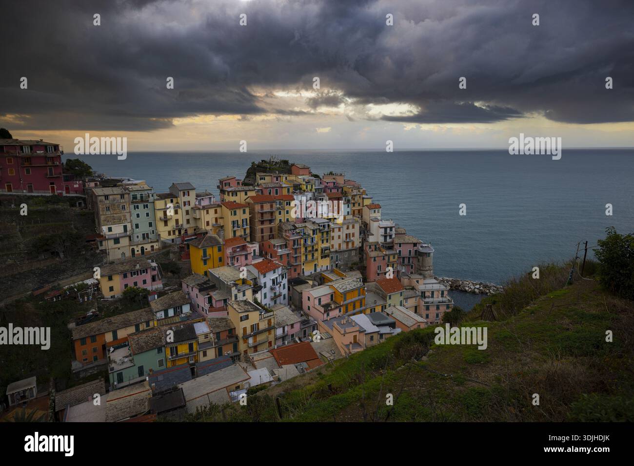 Der Blick auf farbenfrohe Gebäude stürzt unter einem dramatischen, wolkenreichen Himmel zum Meer hinunter und bildet einen lebhaften Kontrast zum tiefblauen Wasser Manaro Stockfoto