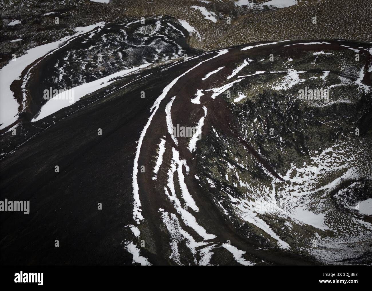 Aus der Vogelperspektive auf die schroffe schwarze vulkanische Erde, die mit strahlend weißem Schnee zerschnitten ist, was eine unüberirdische Landschaft aus Feuer und Eis schafft, Flugir, Rangárþing yt Stockfoto