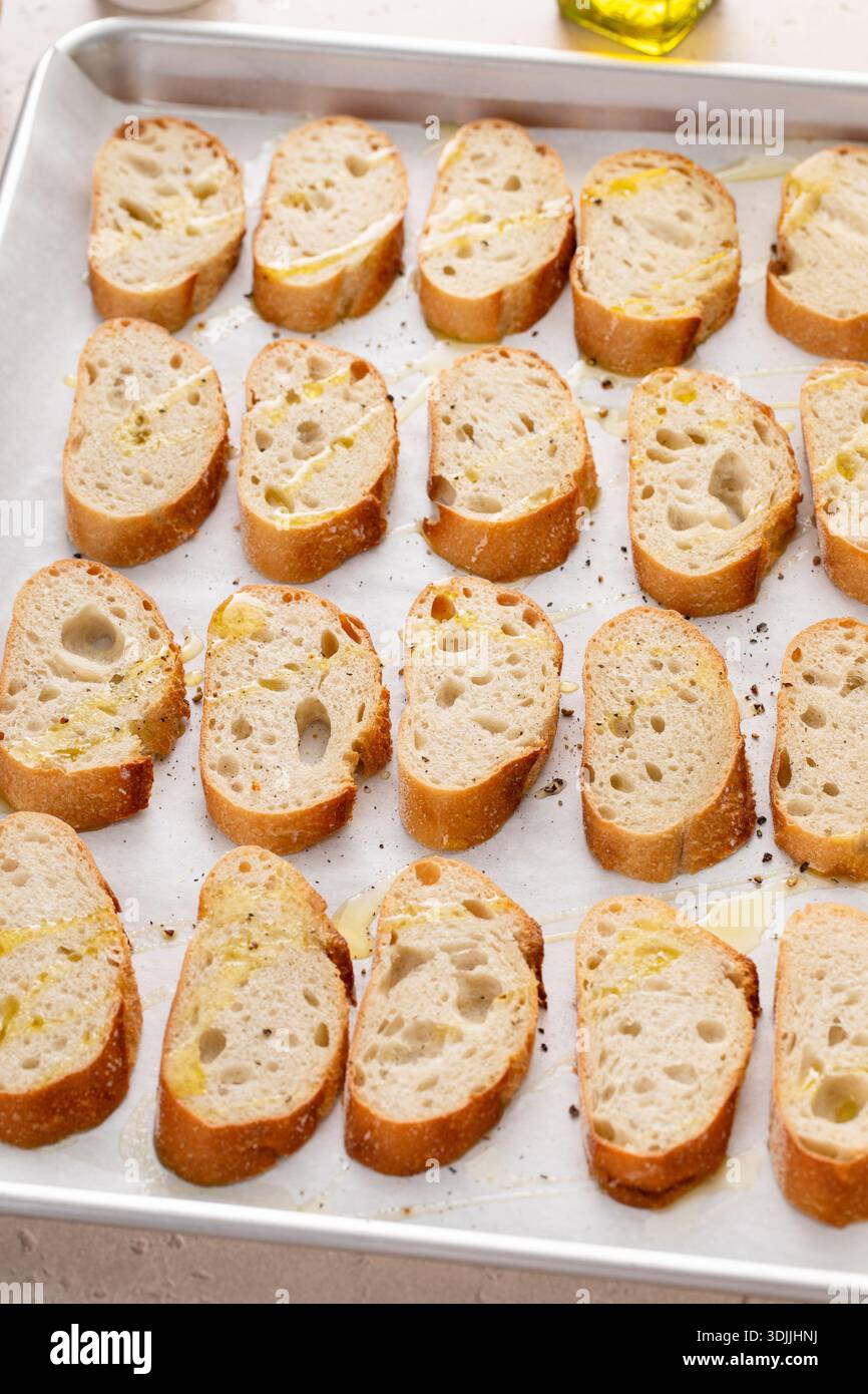 Baguette-Scheiben auf einem Backblech mit Olivenöl, Salz und Pfeffer braten, um Crostini oder Bruschetta zu machen Stockfoto