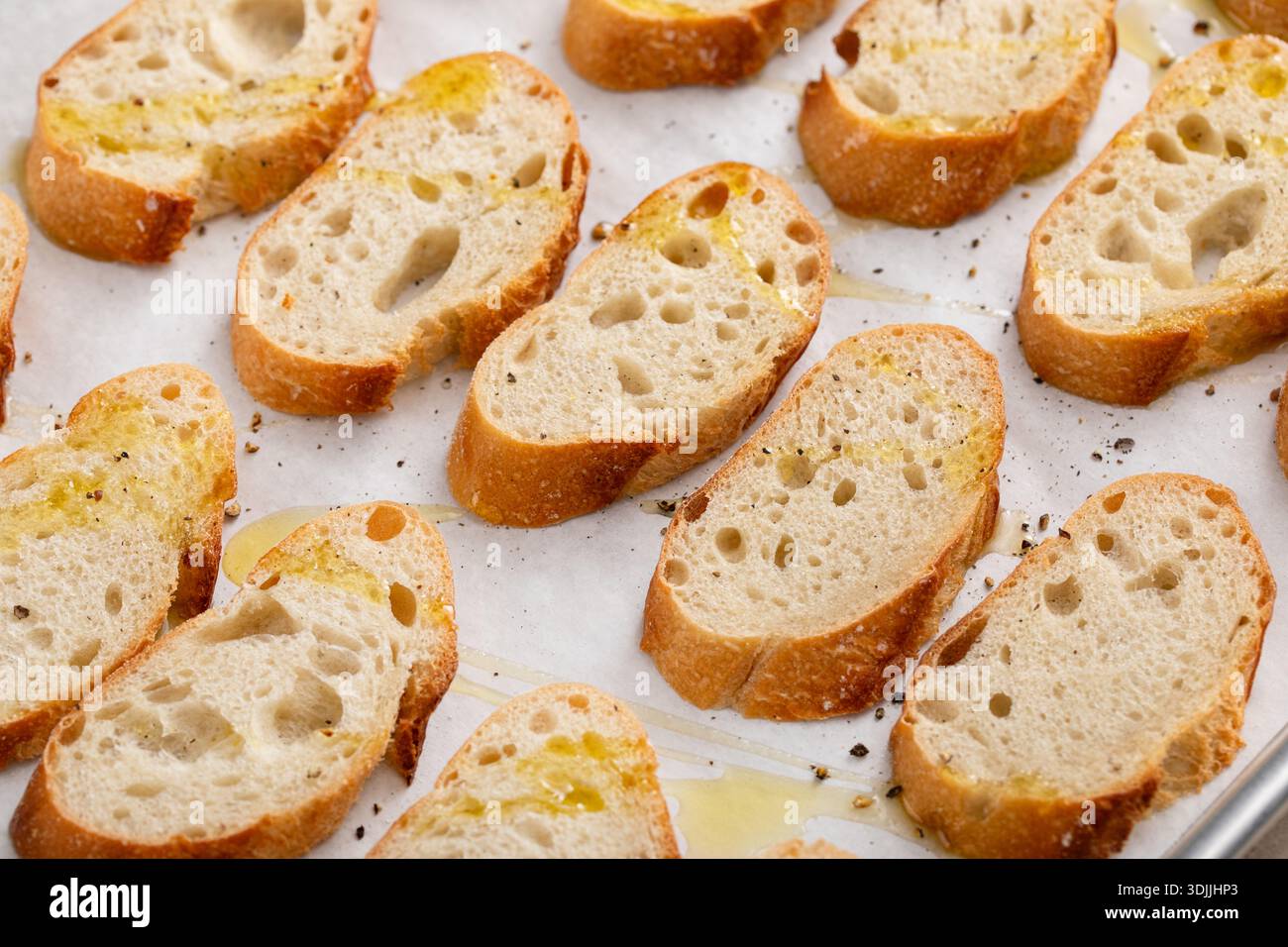 Baguette-Scheiben auf einem Backblech mit Olivenöl, Salz und Pfeffer braten, um Crostini oder Bruschetta zu machen Stockfoto