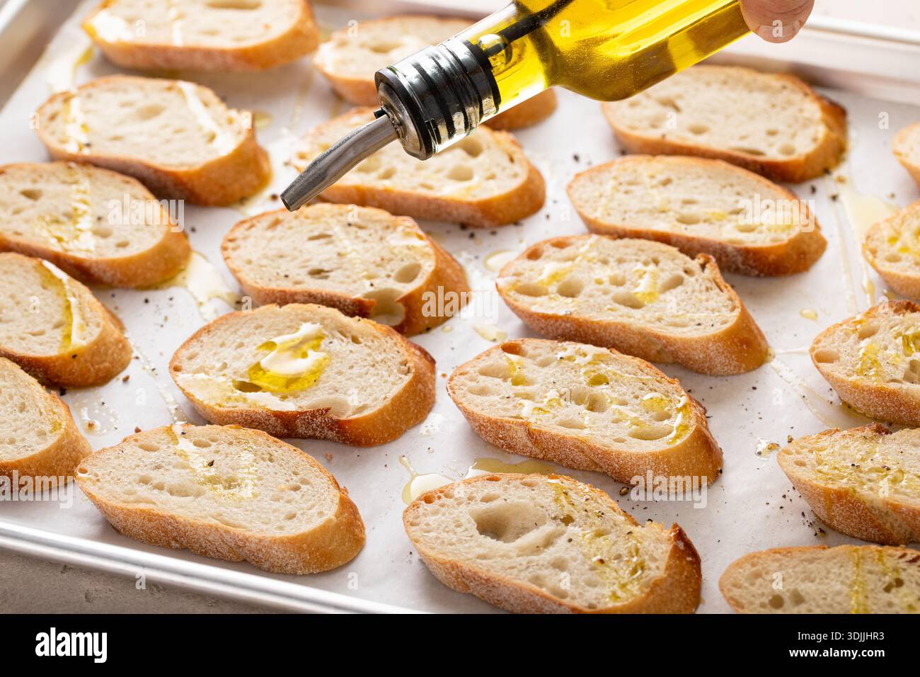 Baguette-Scheiben auf einem Backblech mit Olivenöl, Salz und Pfeffer braten, um Crostini oder Bruschetta zu machen Stockfoto