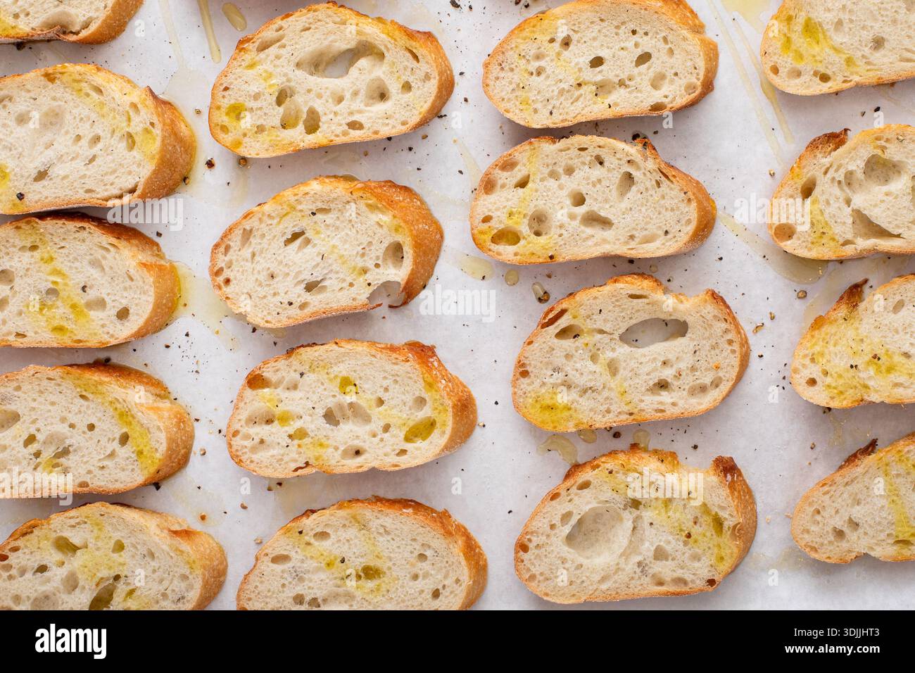 Baguette-Scheiben auf einem Backblech mit Olivenöl, Salz und Pfeffer braten, um Crostini oder Bruschetta zu machen Stockfoto