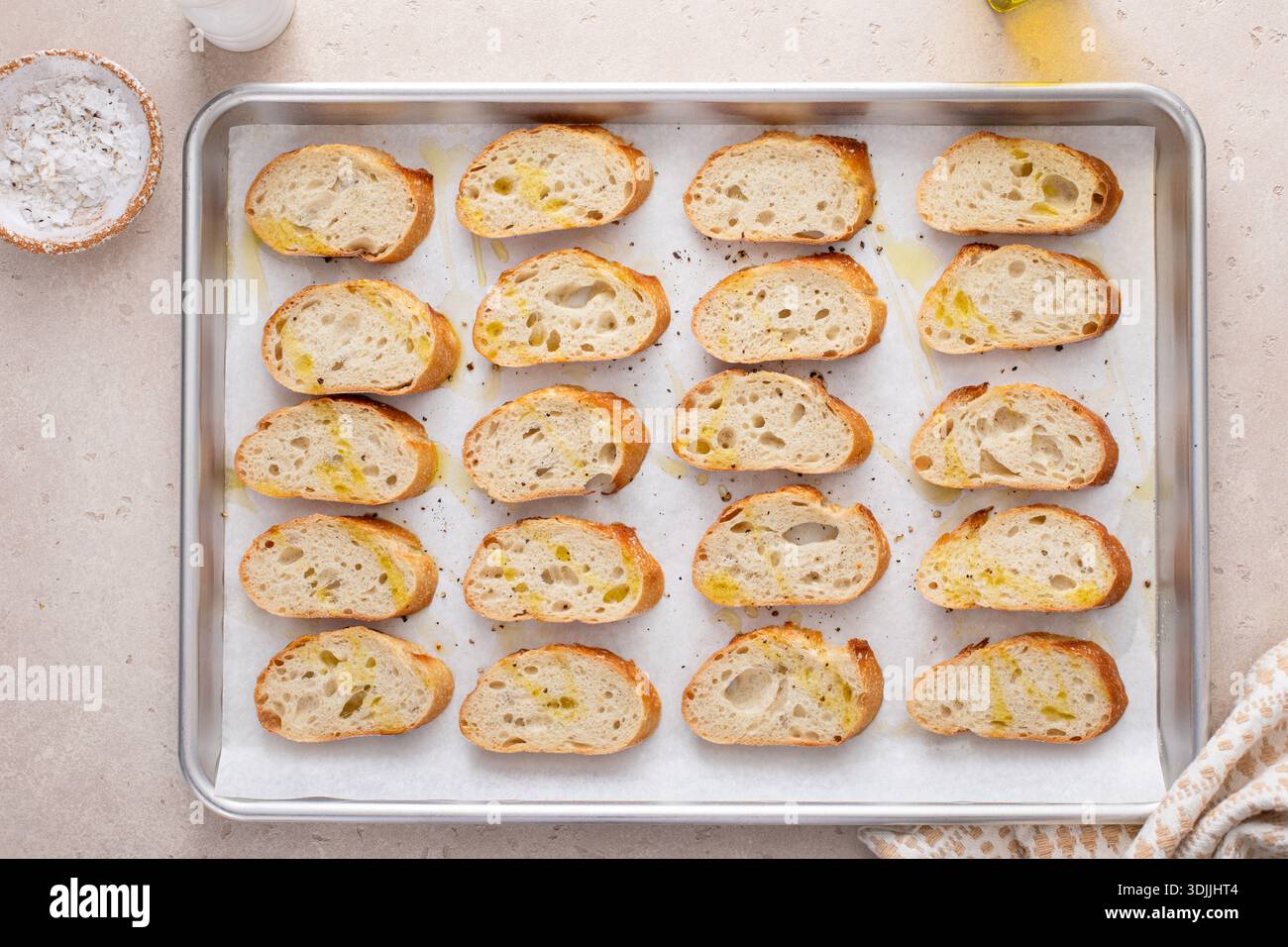 Baguette-Scheiben auf einem Backblech mit Olivenöl, Salz und Pfeffer braten, um Crostini oder Bruschetta zu machen Stockfoto