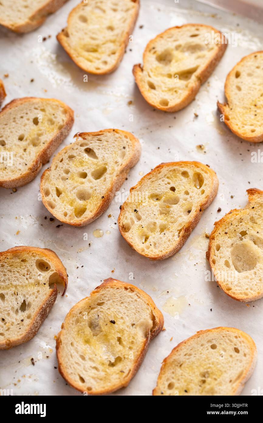 Gebratene Baguetteschnitten auf einem Backblech mit Olivenöl, Salz und Pfeffer zu Crostini oder Bruschetta Stockfoto