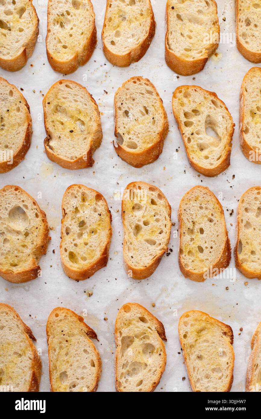 Gebratene Baguetteschnitten auf einem Backblech mit Olivenöl, Salz und Pfeffer zu Crostini oder Bruschetta Stockfoto