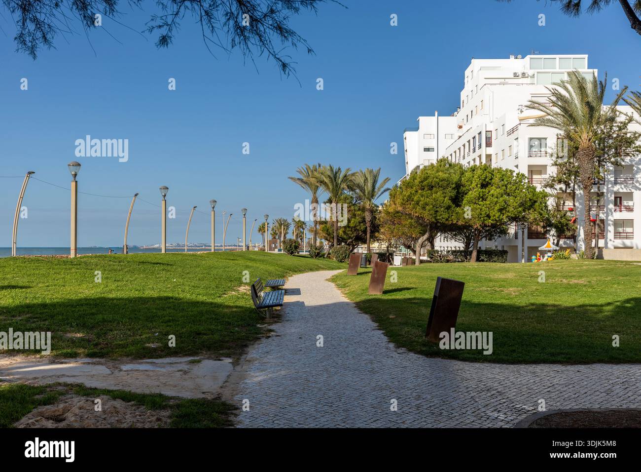 Sonniger Tag in Quarteira, Algarve, Portugal, mit einem üppig grünen Stadtgebiet mit Bäumen, Rasenflächen und Wanderwegen. Entspannender Außenbereich an einer Küste Stockfoto