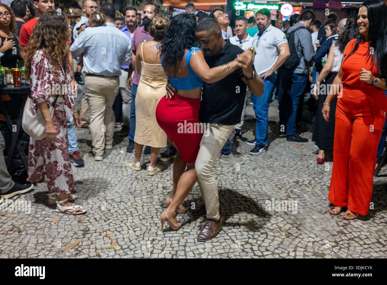 Ein Paar tanzt bei einer Roda de Samba in Cinelândia, im Zentrum von Rio de Janeiro, Brasilien, während eines lebhaften nächtlichen Straßentreffens. Stockfoto