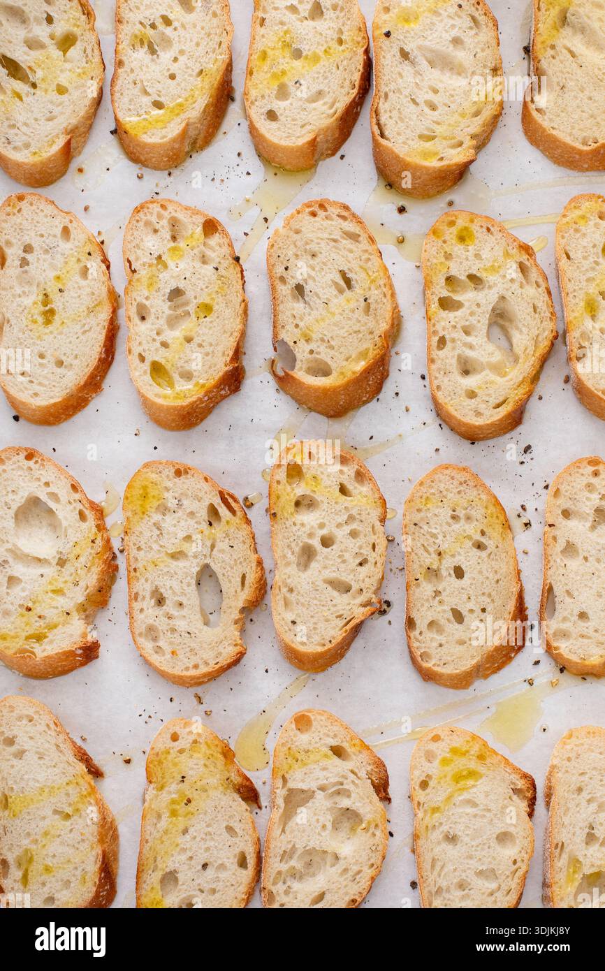 Baguette-Scheiben auf einem Backblech mit Olivenöl, Salz und Pfeffer braten, um Crostini oder Bruschetta zu machen Stockfoto