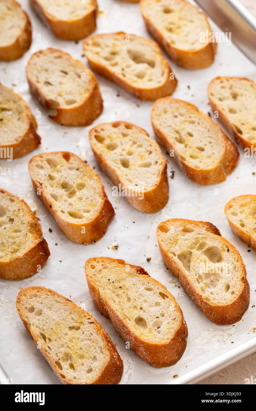 Gebratene Baguetteschnitten auf einem Backblech mit Olivenöl, Salz und Pfeffer zu Crostini oder Bruschetta Stockfoto