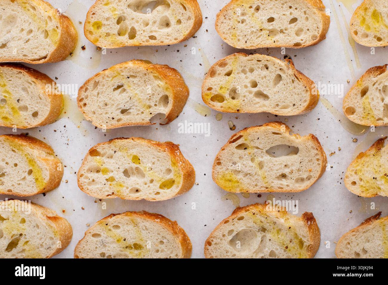 Baguette-Scheiben auf einem Backblech mit Olivenöl, Salz und Pfeffer braten, um Crostini oder Bruschetta zu machen Stockfoto