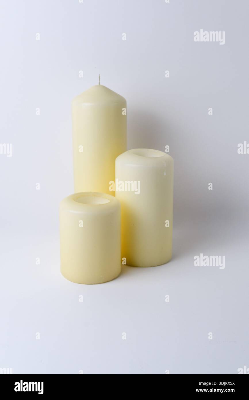 Minimale Stilllebensdauer von drei Kerzen mit elfenbeinfarbenen Säulen, die auf einem klaren hellen Hintergrund unbeleuchtet sind, ideal für Spa- oder Wohnkultur-Konzepte. Stockfoto