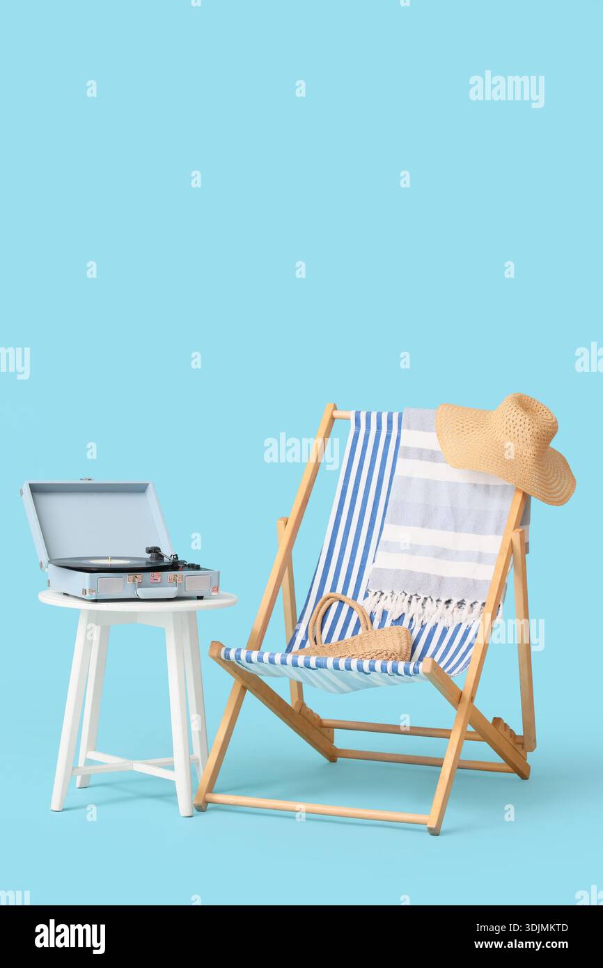 Schallplattenspieler auf Tisch mit Liegestuhl und Strandaccessoires vor blauem Hintergrund Stockfoto
