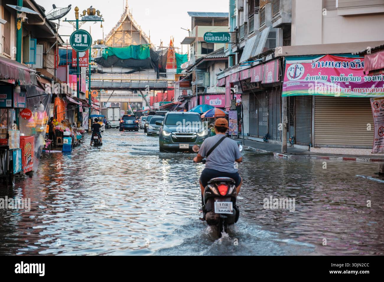 Maeklong Railway Market in Thailand, 5. Dezember 2025, Wasser überschwemmt die Straßen, während Menschen auf Motorrädern durch die überfluteten Straßen fahren Stockfoto