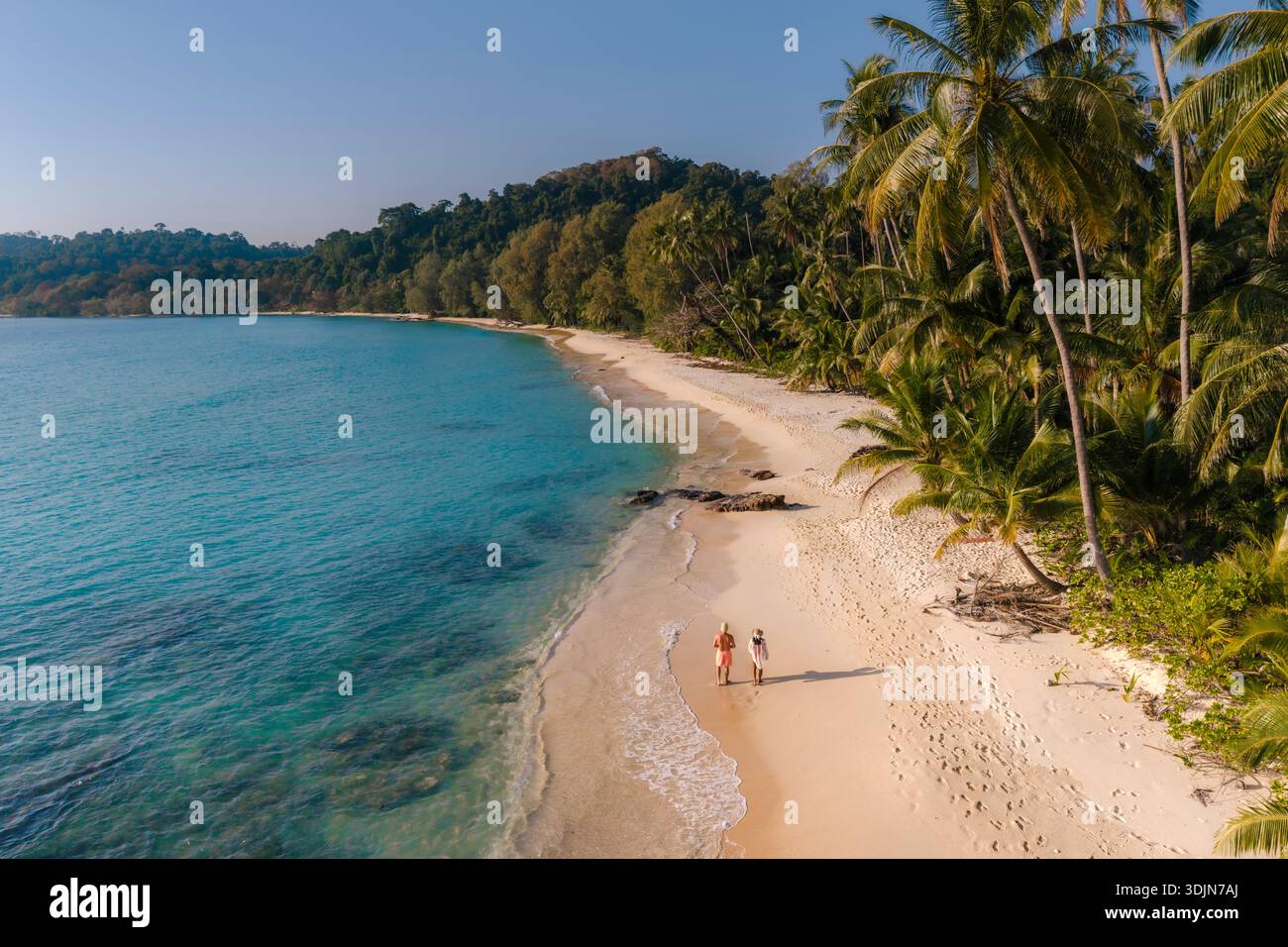 Erleben Sie einen ruhigen Morgen, während zwei Reisende Hand in Hand entlang des weichen Sandes von Takhian Beach gehen, umgeben von wogenden Palmen und Kristallkellen Stockfoto
