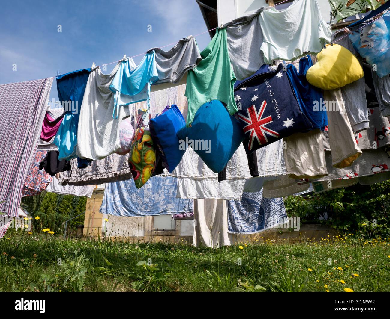 Verschiedene Kleidung, bunte Kissen und eine große blaue Tasche mit der australischen Flagge, die in einem sonnigen Garten an einer Wäscheleine hängt Stockfoto