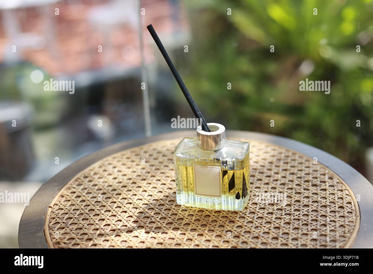 Ruhiger Schilfdiffusor mit ätherischem Öl für Aromatherapie, natürlicher Duft für Wohnkultur für entspannendes Wohlbefinden. Glasflasche auf Rattantisch mit g Stockfoto