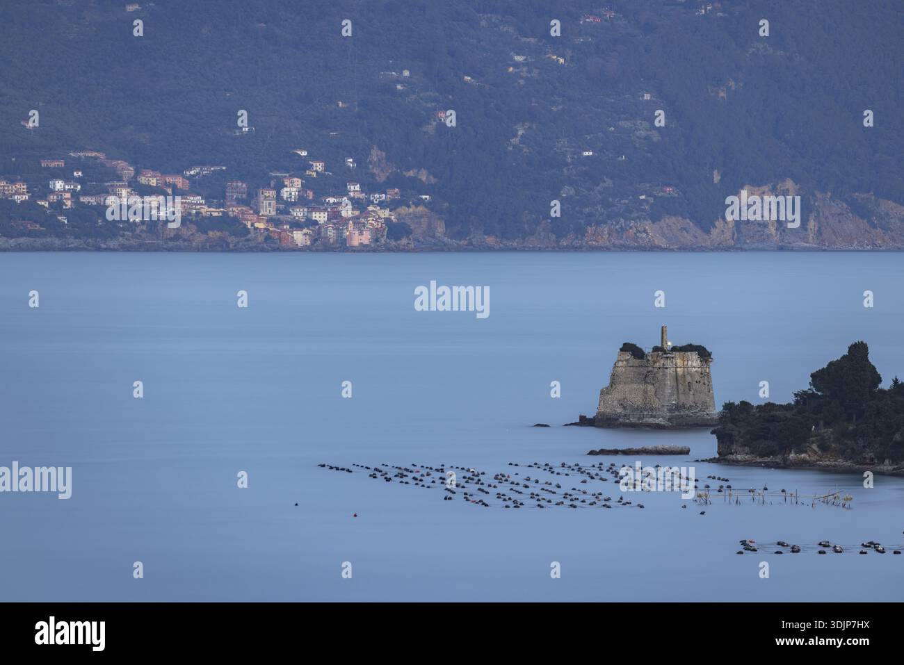 Blick auf eine ruhige Meereslandschaft mit einer felsigen Insel, gekrönt von einem Leuchtturm, umgeben von ruhigem blauem Wasser, Porto Venere, Ligurien, Italien. Stockfoto