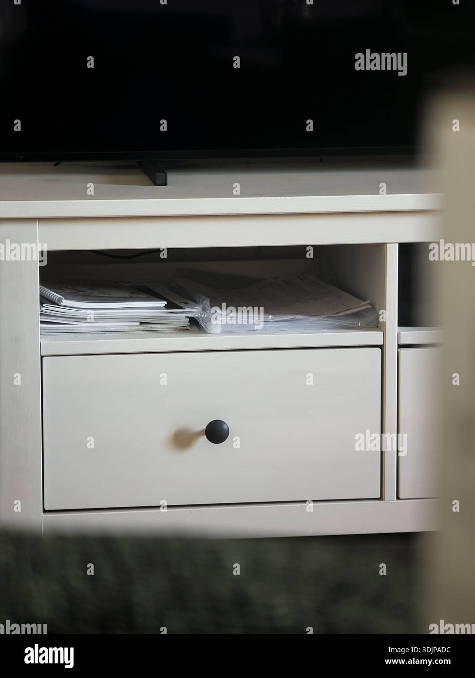 Ein sauberer, weißer TV-Standfuß mit einer einzigen Schublade und einem offenen Regal bietet Platz für verstreute Papiere, was den täglichen Einsatz im Home Office in einem ruhigen, organisierten Leben nahelegt Stockfoto