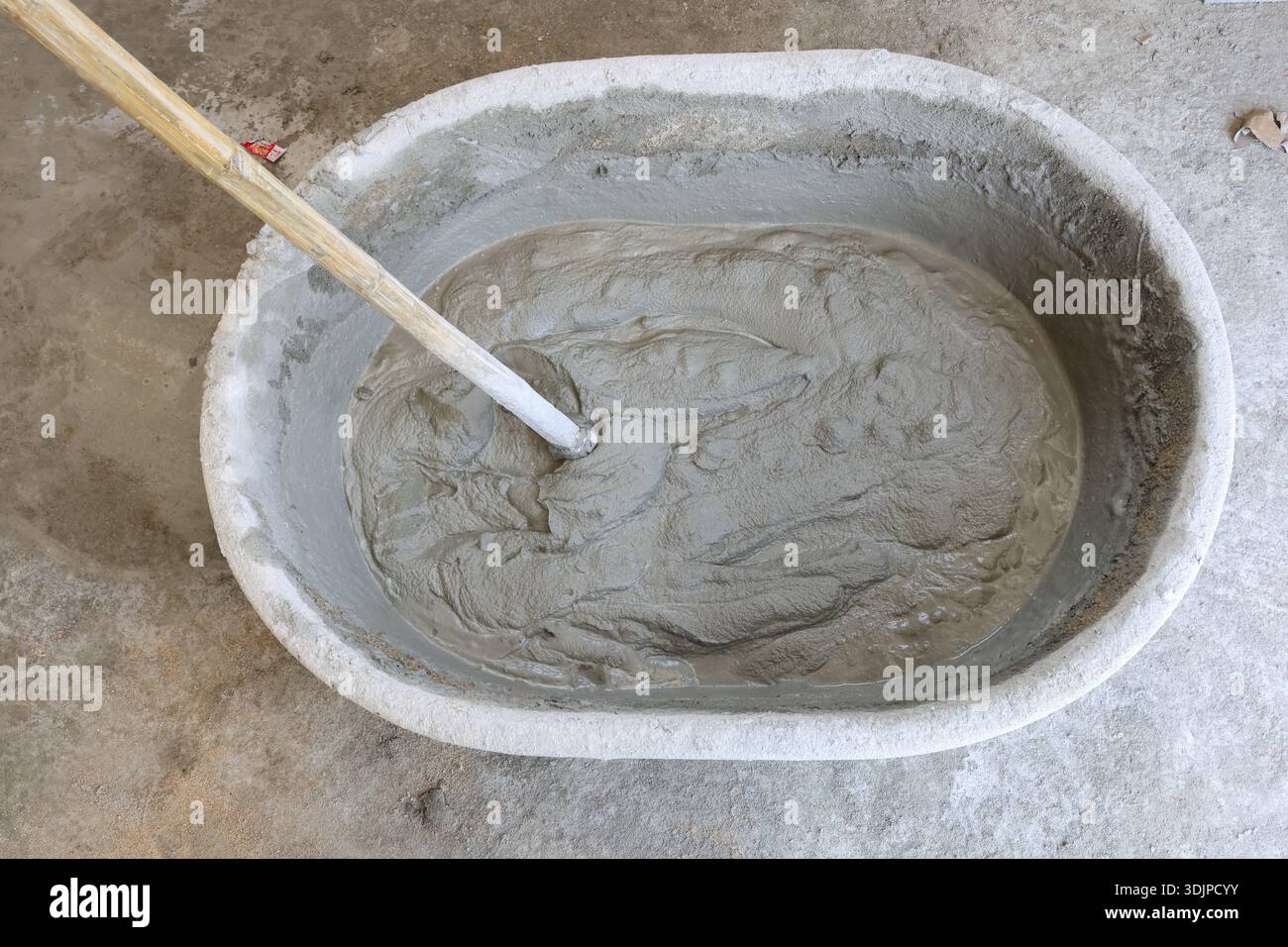 Feuchter Zementmörtel in Kunststoffeimer mit Holzhacke für Bauarbeiten, die für Reparatur- und Renovierungsprojekte vorbereitet sind Stockfoto