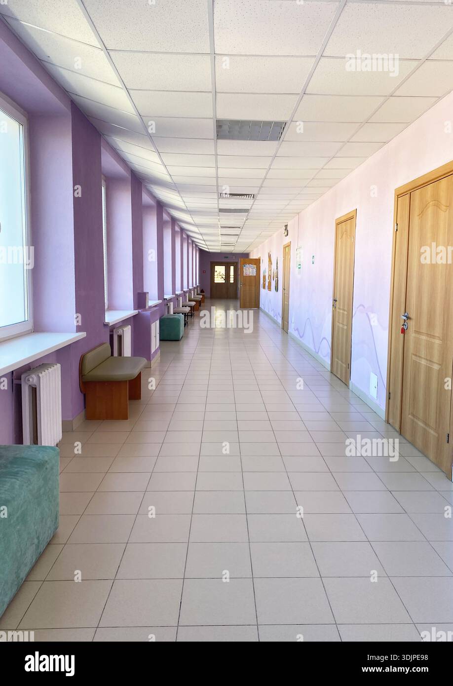 Geräumiger Korridor mit violetten Wänden und großen Fenstern, mit Bänken an den Seiten, die eine einladende Umgebung für Besucher und Bewohner schaffen Stockfoto