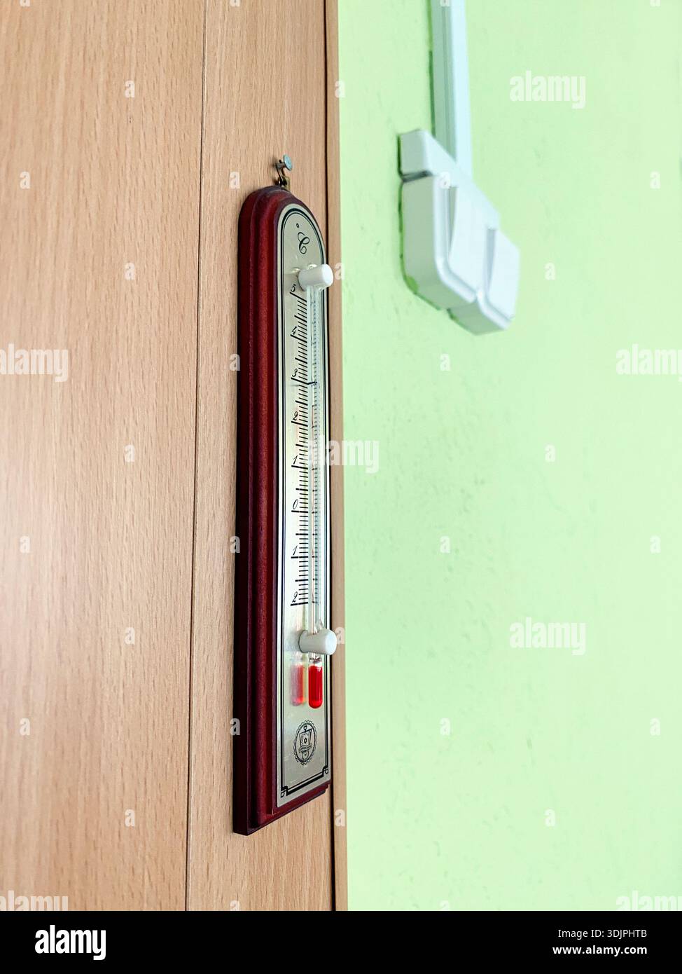 Thermometer, das an einer Holzwand angebracht ist, in einer lehrreichen Umgebung, das Temperaturwerte mit einer grünen Wand im Hintergrund anzeigt Stockfoto