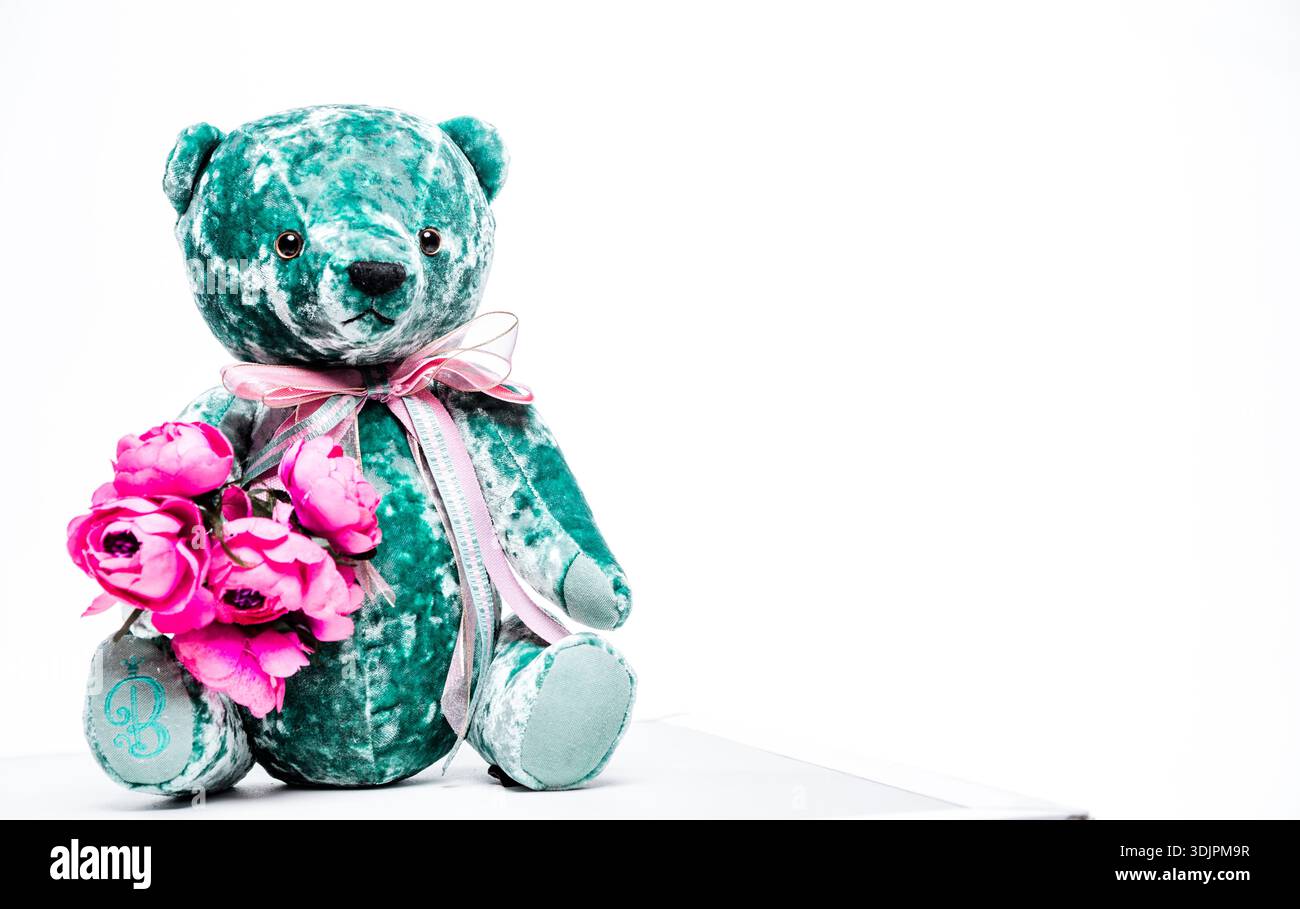 Teal Plüschteddybär mit rosafarbenen Blumen, verziert mit einem Band, auf einem sauberen weißen Hintergrund, geeignet für Kinderspielzeug und Geschenke Stockfoto
