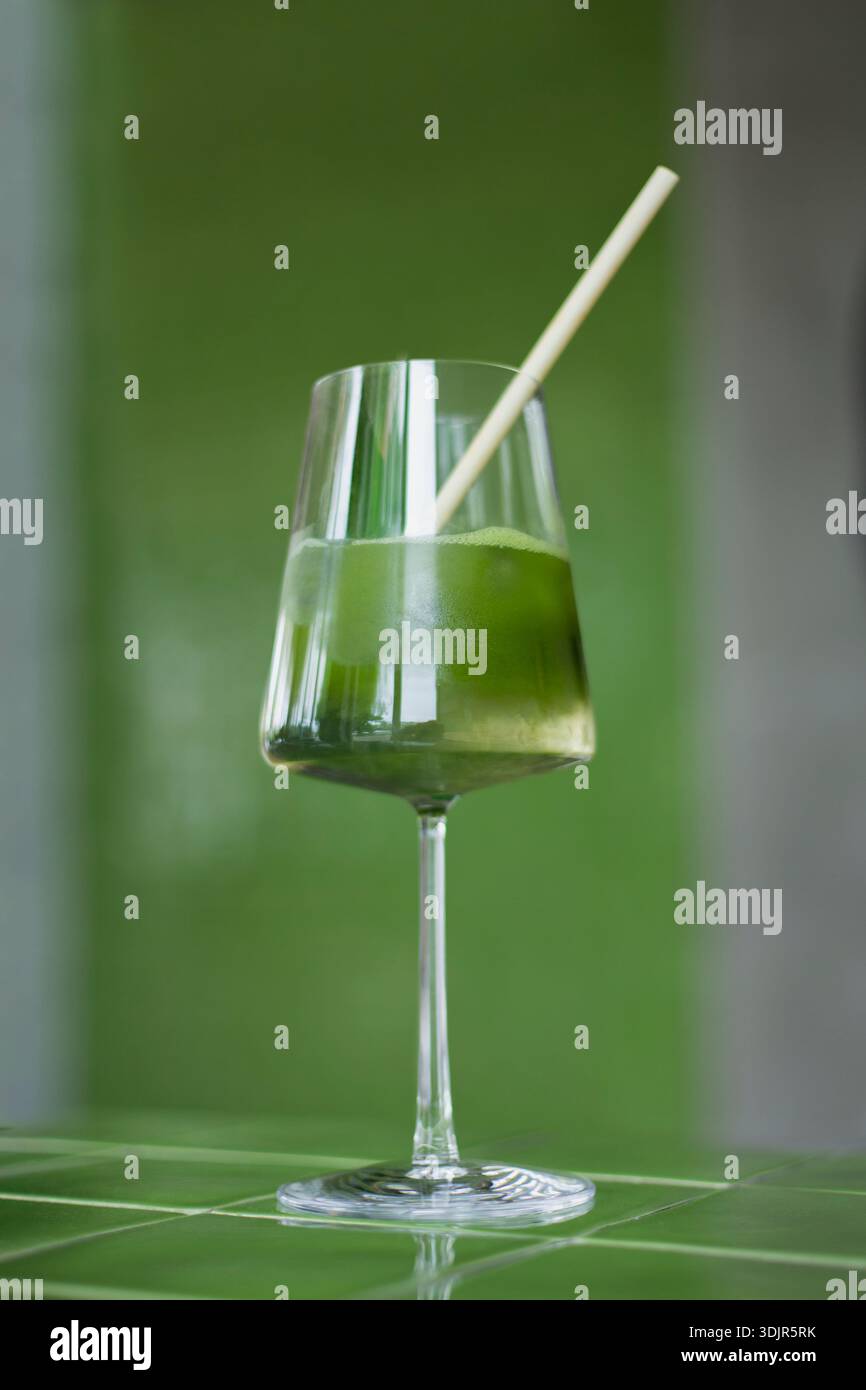 Japanische Eismatcha Latte, grüner Tee mit Milch, Sojamilch, traditionelle Matcha-Werkzeuge, mit Bambusstroh im Glas auf grünem Hintergrund. Cocktail i Stockfoto