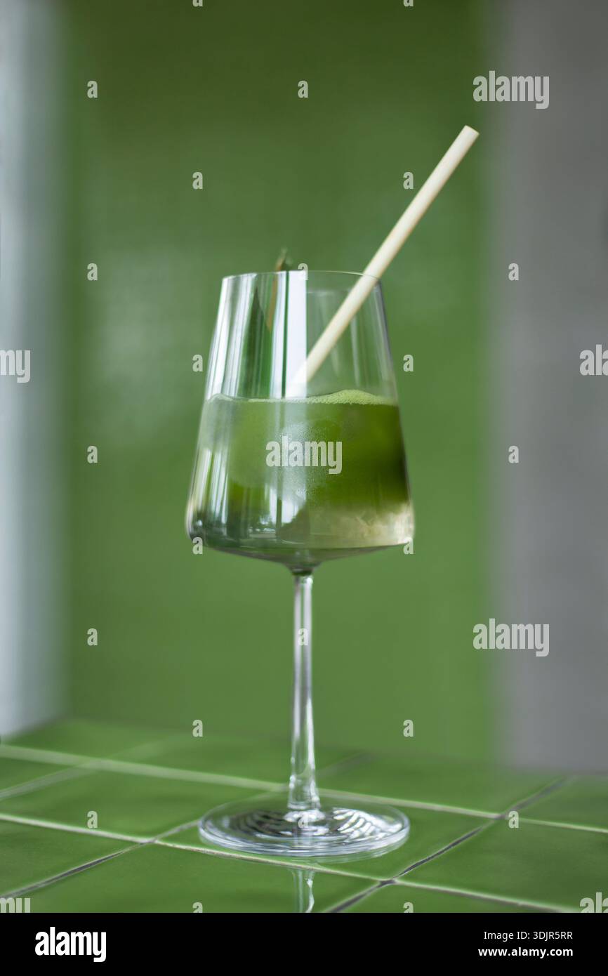 Japanische Eismatcha Latte, grüner Tee mit Milch, Sojamilch, traditionelle Matcha-Werkzeuge, mit Bambusstroh im Glas auf grünem Hintergrund. Cocktail i Stockfoto