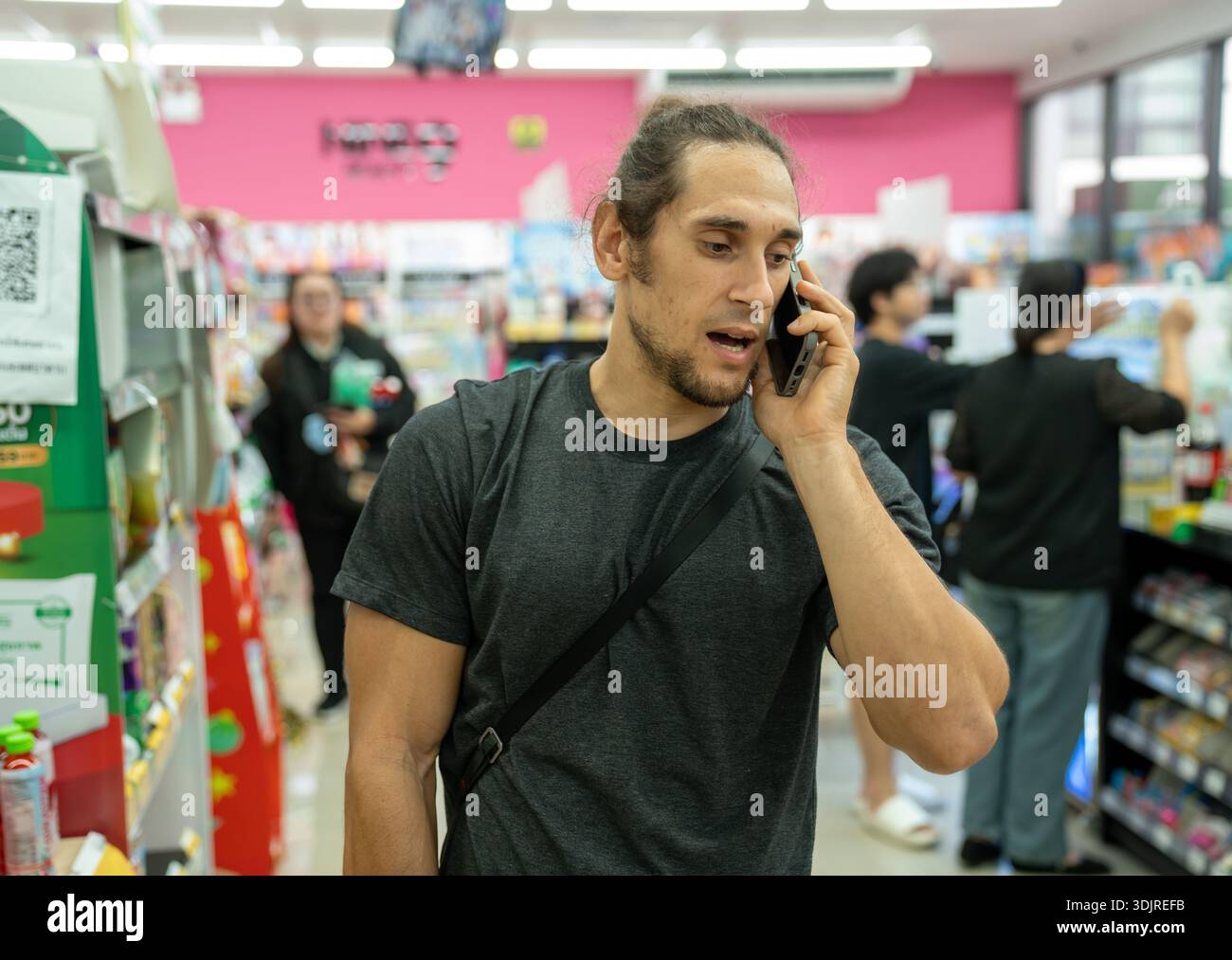 Junger Mann, der am Telefon im Supermarktgang spricht Stockfoto