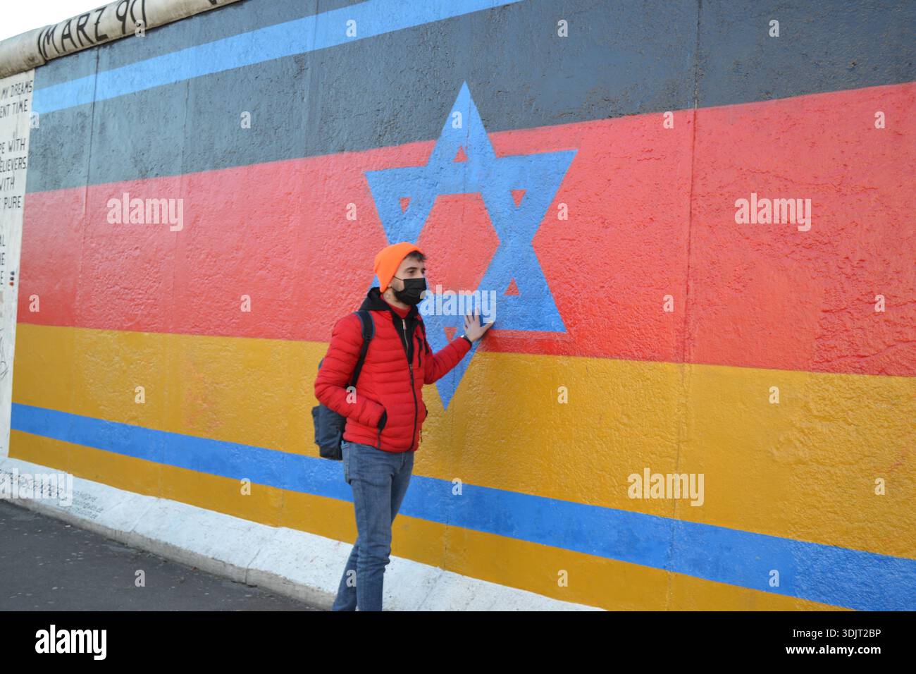 Berlin, Deutschland – Besucher posiert vor einem Wandgemälde in der East Side Gallery, einem historischen Teil der Berliner Mauer. Stockfoto
