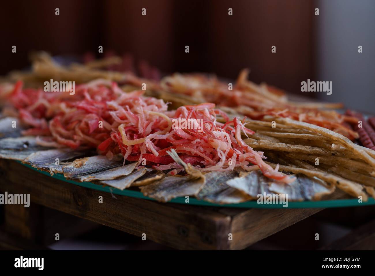 Eine rustikale Holzplatte zeigt ein appetitliches Arrangement aus dünn geschnittenem eingelegtem Gemüse und getrocknetem Fisch, das kräftige Rot- und Gelbtöne zeigt Stockfoto