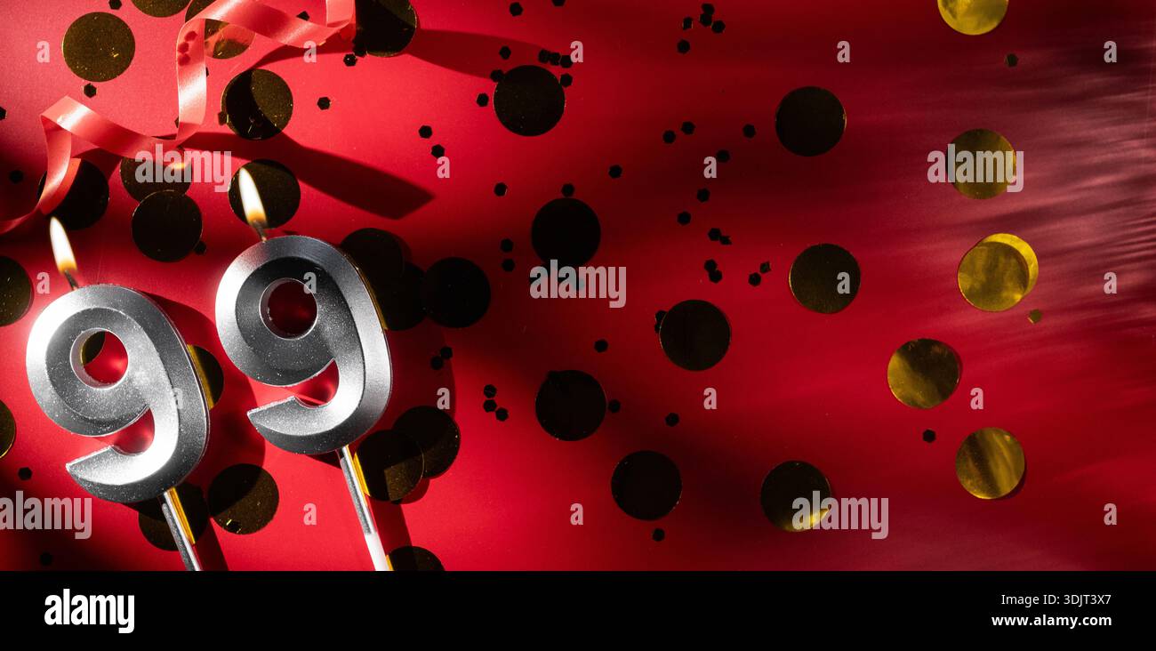 Konzept der Geburtstagsfeier und Jubiläumsfeier. Nummer 99 neunundneunzig silberne Geburtstagskerze auf festlichem rotem Hintergrund mit großem goldenen Hintergrund Stockfoto