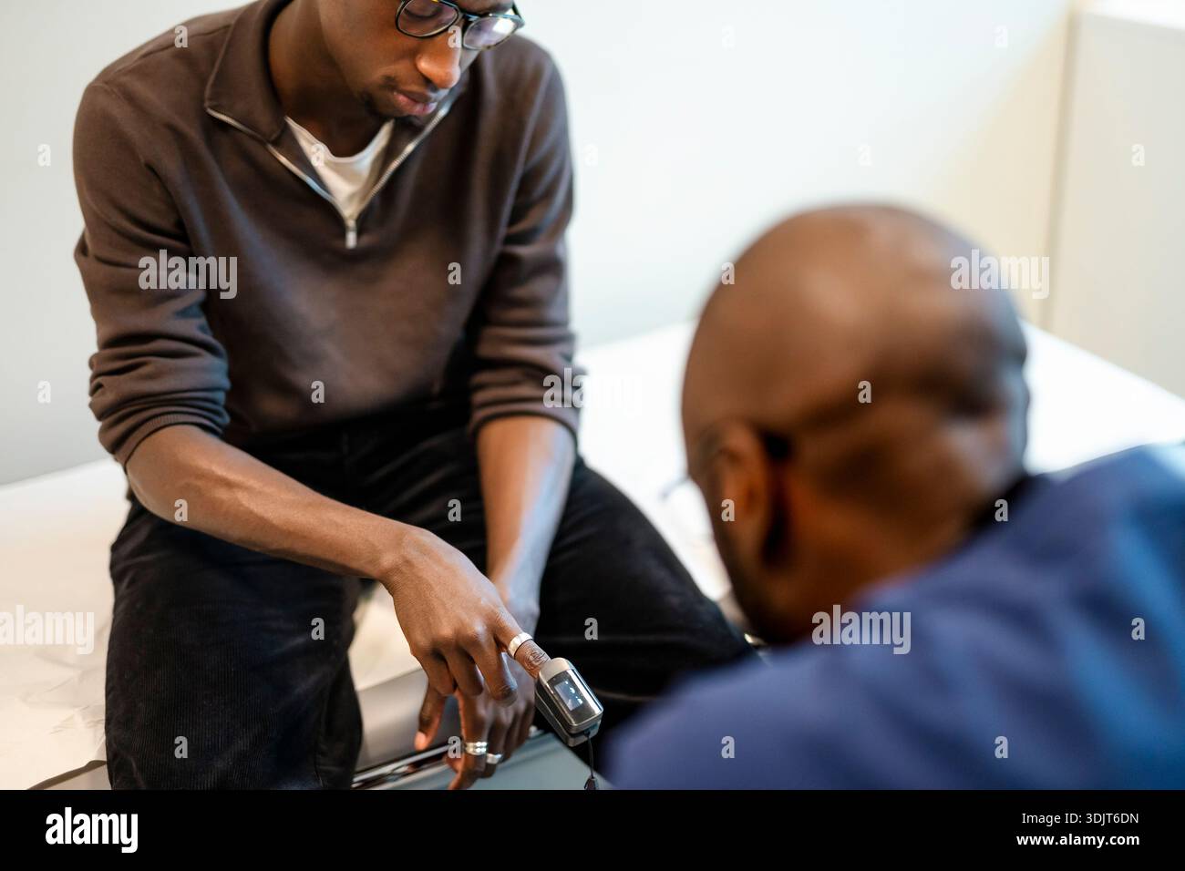 Hochwinkelansicht eines jungen Mannes, der mit Oximeter am Finger sitzt, während eines Krankenhausbesuchs Stockfoto