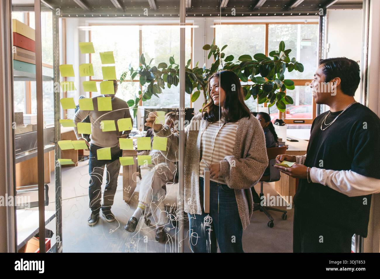 Lächelnde weibliche Designerin, die während der Besprechung in einem neuen Büro Ideen an Glastüren schreibt Stockfoto