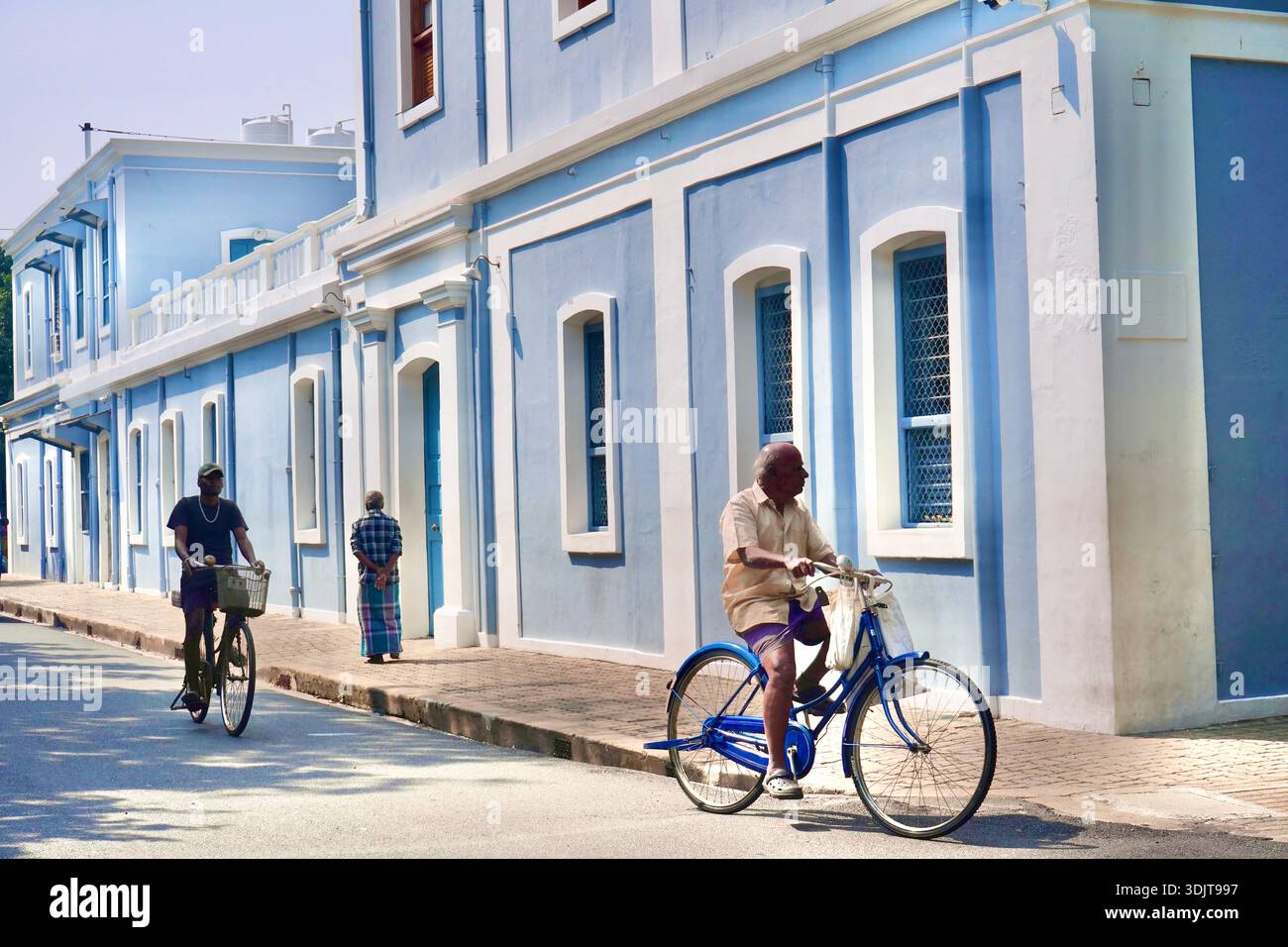 Älterer Mann radelt an pastellblauen französischen Kolonialgebäuden in Puducherry’s White Town, Indien Stockfoto
