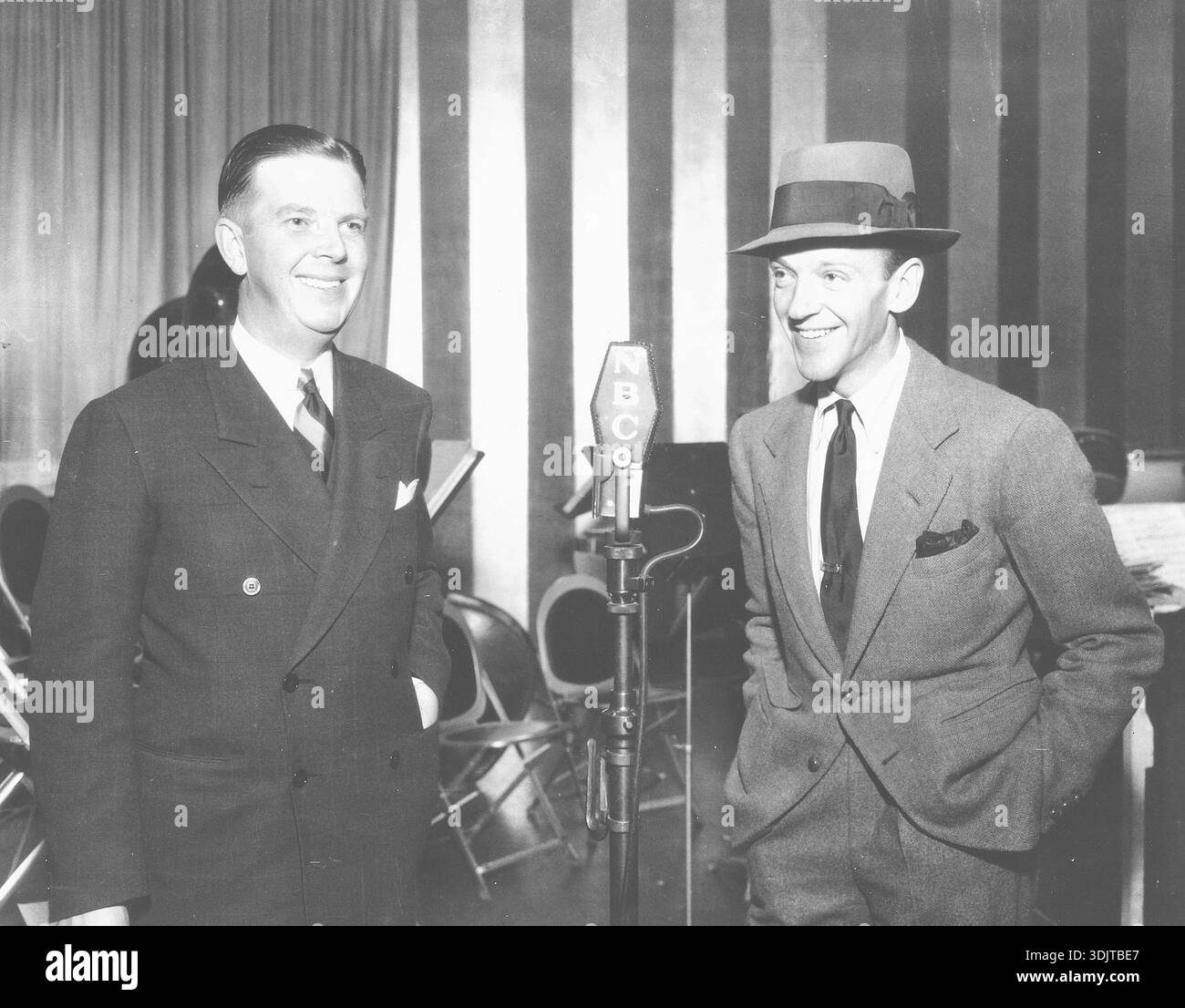 Fred Astaire und Ken Carpenter, Ass-Radiosprecher von NBC, entspannen sich im Dezember 1936 im NBC-Red Network Studio in Hollywood, Kalifornien. Sie machten die Radiosendung "The Packard Hour", gesponsert von der Packard Motor Company. Die Show wurde jeden Dienstag von 21:30 bis 22:30 Uhr Eastern Standard Time live gespielt. Fred Astaire gab sein Debüt als regelmäßiger Radiomoderator in dieser Sendung, in der er sang, gelegentlich Tap Dancing „on the Air“ und komödiantische Skizzen zeigte. Stockfoto