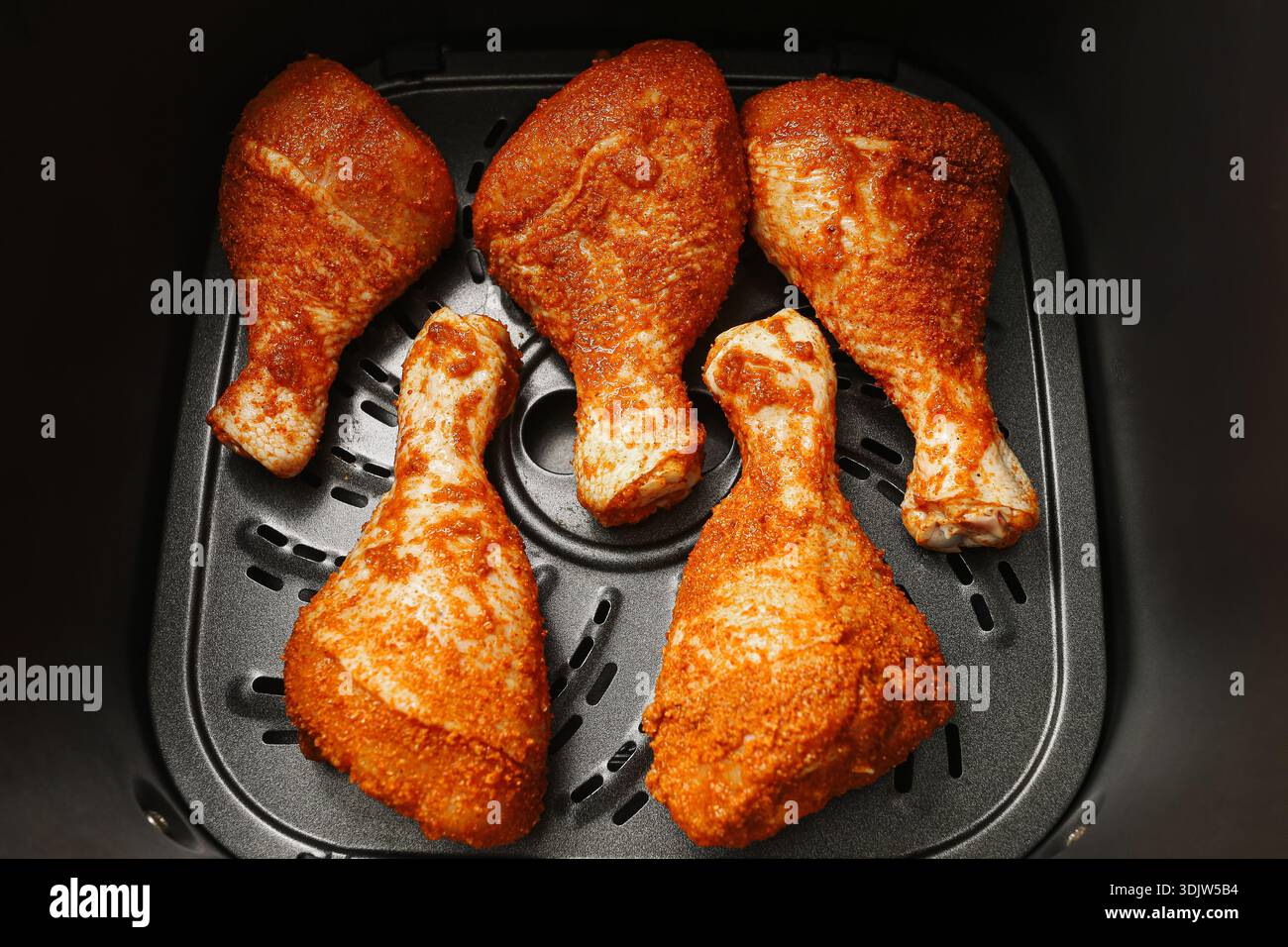Gewürzte rohe Hähnchenkeulen, die vor dem Kochen in einen Korb der Fritteuse gelegt werden. Hausküche Mahlzeit Zubereitung mit Geflügelfleisch. Moderne Kochgeräte. Stockfoto